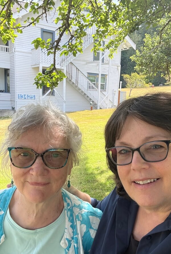 two women in front of a white house